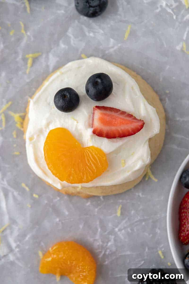 A colorful Crumbl-style frosted fruit pizza cookie, adorned with fresh fruits and creamy lemon cream cheese frosting.