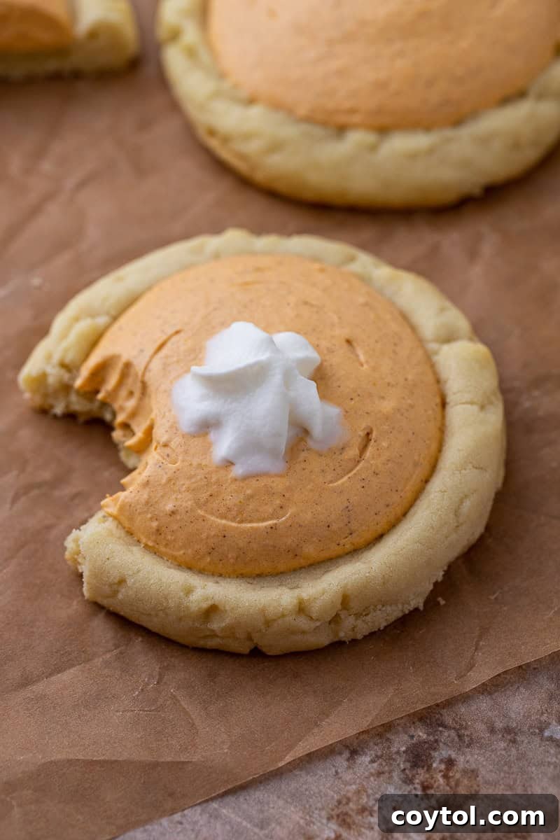 A delectable Crumbl-style pumpkin pie cookie with a bite taken out, revealing its creamy pumpkin filling and whipped cream topping.