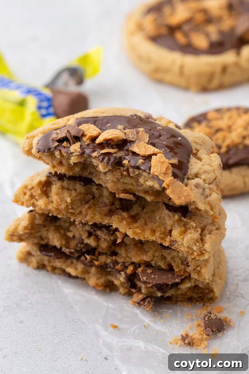 Stacked Crumbl-style Butterfinger peanut butter cookies, showcasing a soft, chewy center with melted chocolate and crunchy Butterfinger pieces.