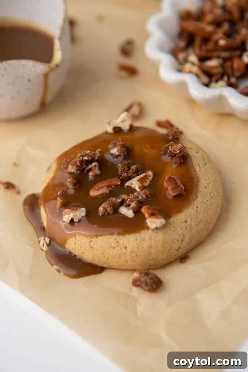 Delicious Crumbl-style Sticky Bun Cookies, spiced sugar cookies topped with brown-sugar caramel frosting and pecan crunch.
