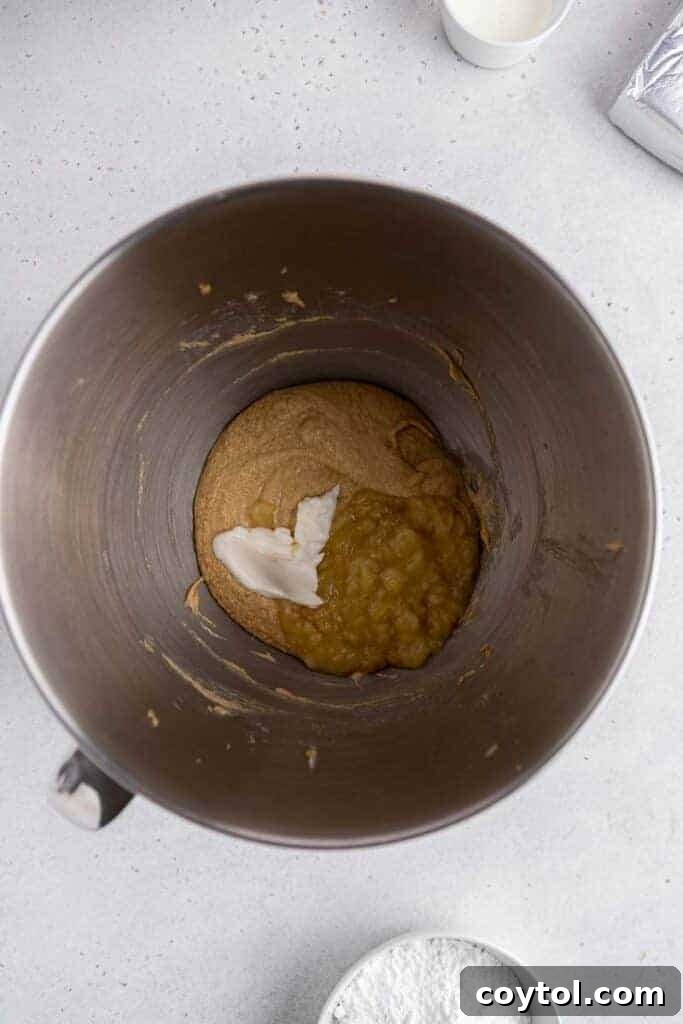 Sour cream being added to the creamed butter mixture, showing the blending of wet ingredients.