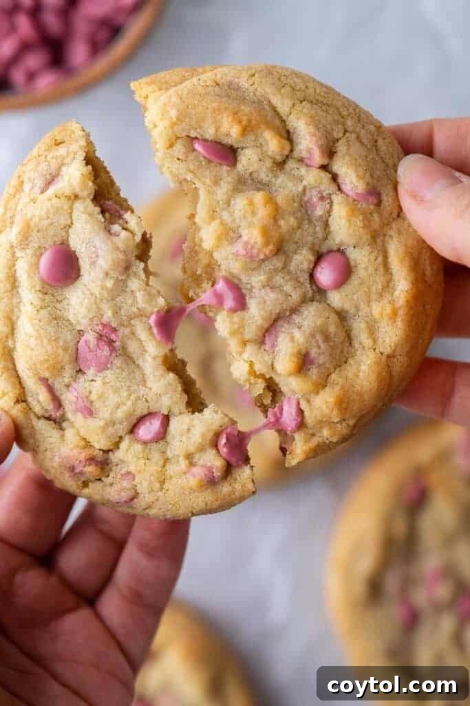 Hand breaking a ruby chocolate cookie in half, revealing its chewy interior