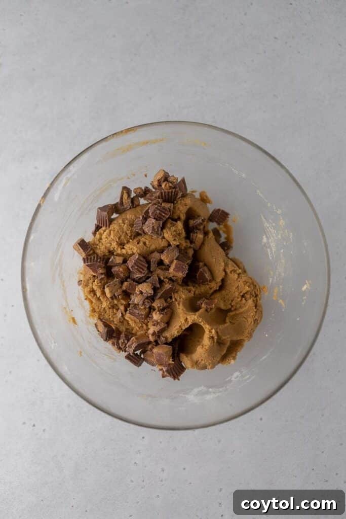 Peanut butter cookie dough in a bowl after dry ingredients and Reese's cups are folded in.