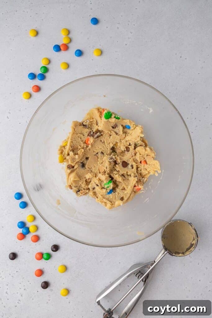 A bowl of vibrant cookie dough, rich with M&M's, peanut butter chips, and chocolate chips, ready for baking.