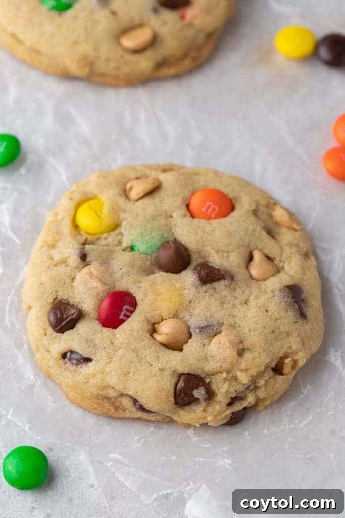 A close-up of a beautifully baked, thick and chewy Crumbl monster cookie resting on parchment paper.