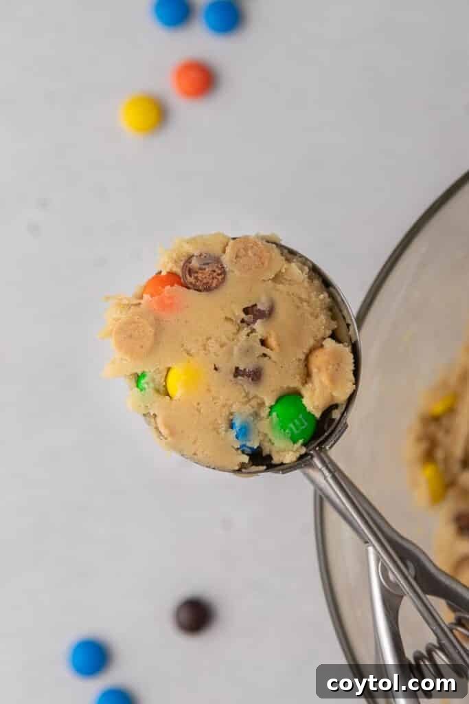 A delectable Crumbl Monster Cookie captured in a cookie scooper, showcasing its rich texture and generous mix-ins.