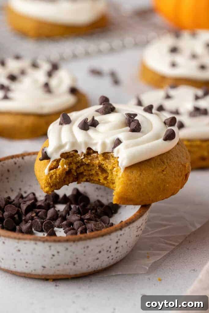 A delicious Crumbl pumpkin cake cookie with a bite taken out, showing the moist interior and creamy frosting