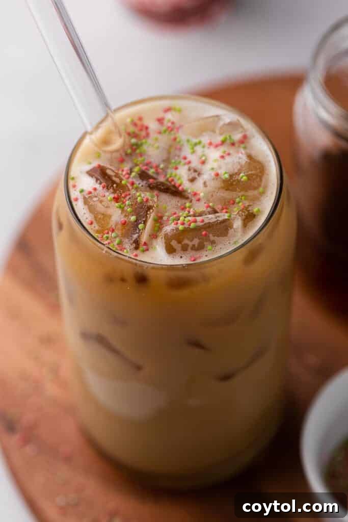 Homemade Starbucks Sugar Cookie Latte with Almond Milk 2 A festive Starbucks Sugar Cookie Almond Milk Latte, featuring a delicate foam topping and colorful sprinkles, served in a clear glass on a cozy holiday-themed background.