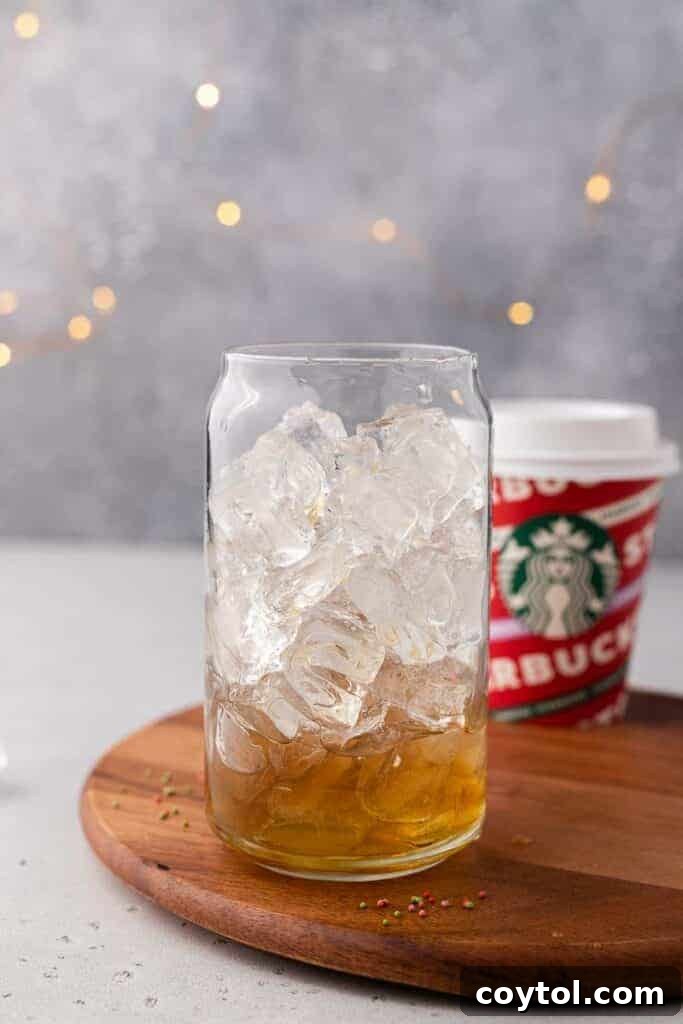 Homemade Starbucks Sugar Cookie Latte with Almond Milk 5 A glass filled with ice and golden sugar cookie simple syrup, ready for a latte creation.
