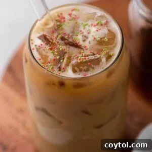 Homemade Starbucks Sugar Cookie Latte with Almond Milk 9 A frothy Starbucks Sugar Cookie Almond Milk Latte, adorned with festive sprinkles, served in a clear glass.