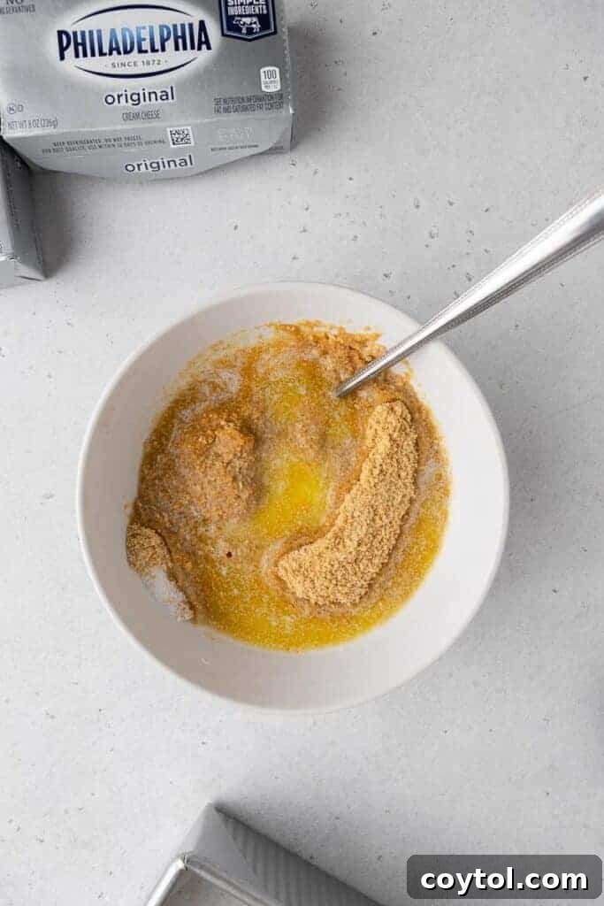 Crushed graham crackers being mixed with melted butter and spices.