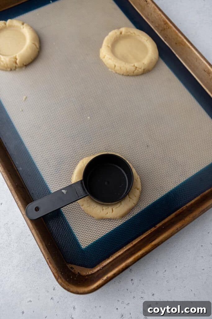 Bakery-Perfect Crumbl Pecan Pie Cookies Homemade 7 Using a 1/4 cup measuring cup to press an indent in cookie dough for pecan pie filling, demonstrating the technique.