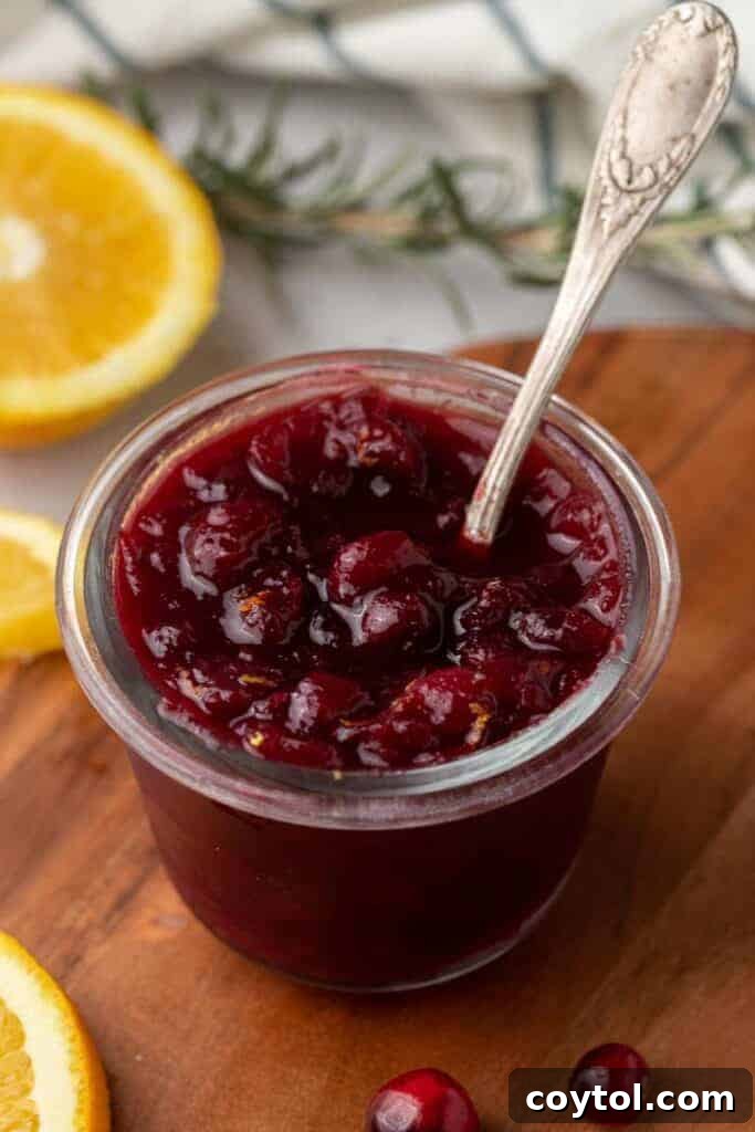 A jar of homemade cranberry sauce with oranges, garnished and ready to serve.