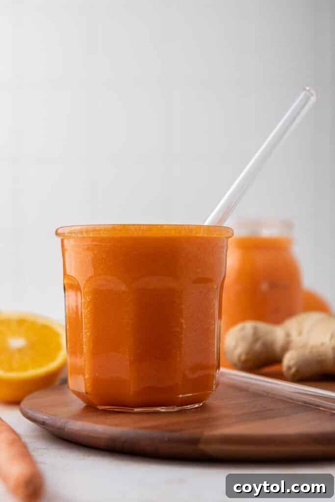 Golden Glow Immune Support Smoothie 2 A vibrant orange carrot ginger smoothie served in a clear glass, garnished with a slice of fresh orange.