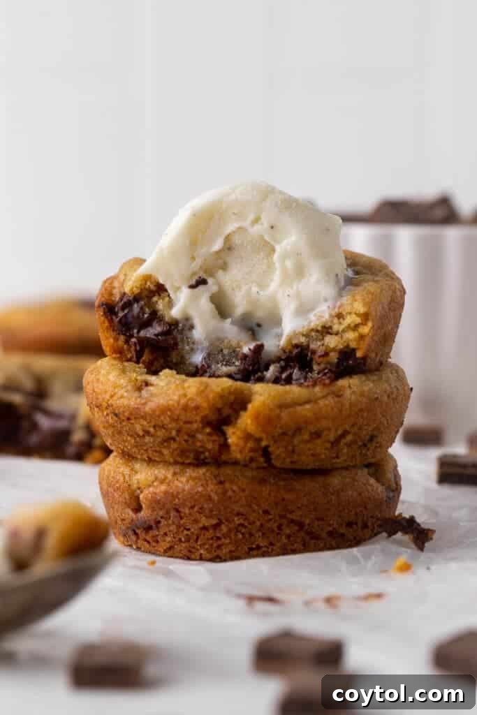 Delightful Mini Crumbl Chocolate Chip Cookie Cups 12 A warm chocolate chip cookie cup topped with a scoop of melting vanilla ice cream and a drizzle of chocolate syrup, creating a perfect dessert experience.