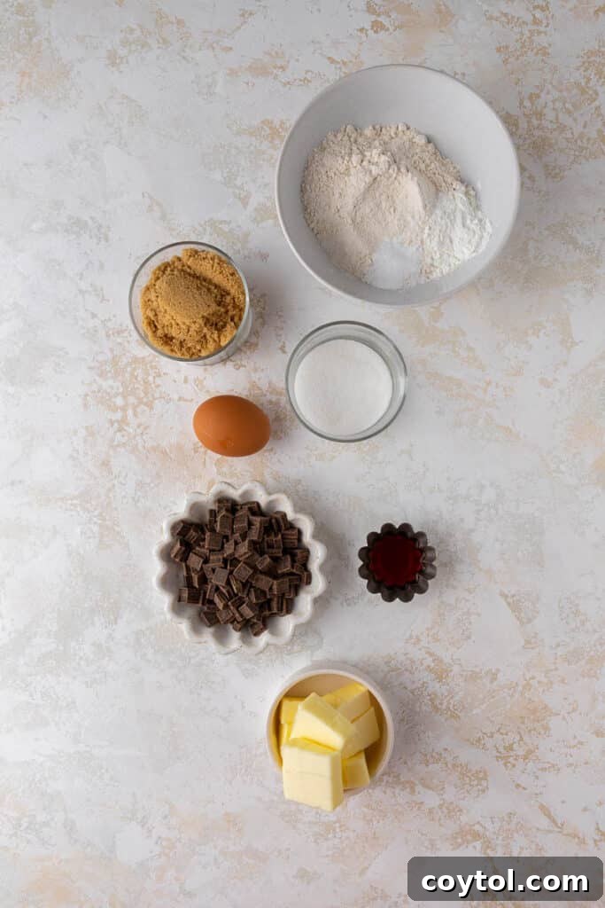 Delightful Mini Crumbl Chocolate Chip Cookie Cups 3 Assortment of fresh ingredients for baking Crumbl-style cookie cups, including butter, sugars, eggs, flour, and semi-sweet chocolate chunks, laid out on a wooden surface.