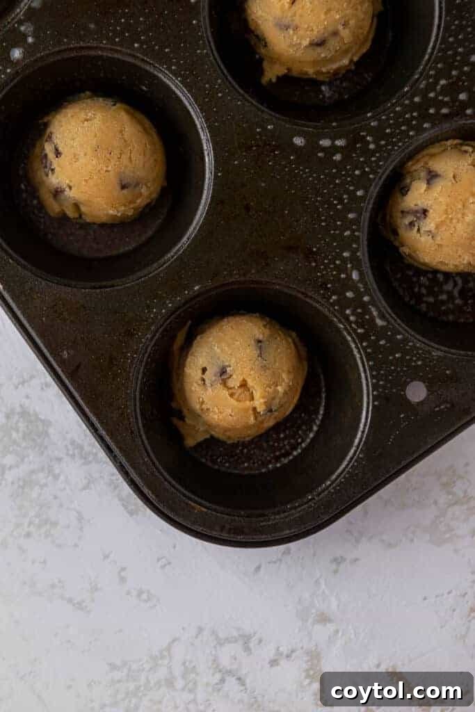 Delightful Mini Crumbl Chocolate Chip Cookie Cups 7 A muffin tin filled with unbaked cookie dough balls, positioned evenly in each cup before baking.