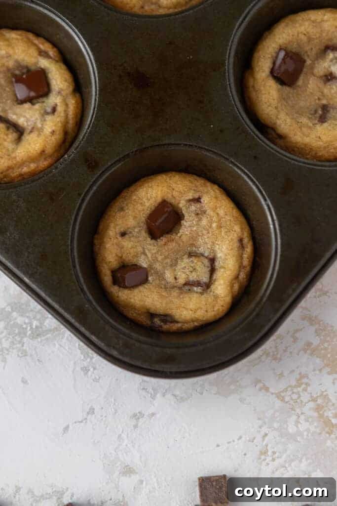 Delightful Mini Crumbl Chocolate Chip Cookie Cups 8 Golden-brown cookie cups freshly baked and still in the muffin tin, cooling slightly after being removed from the oven.