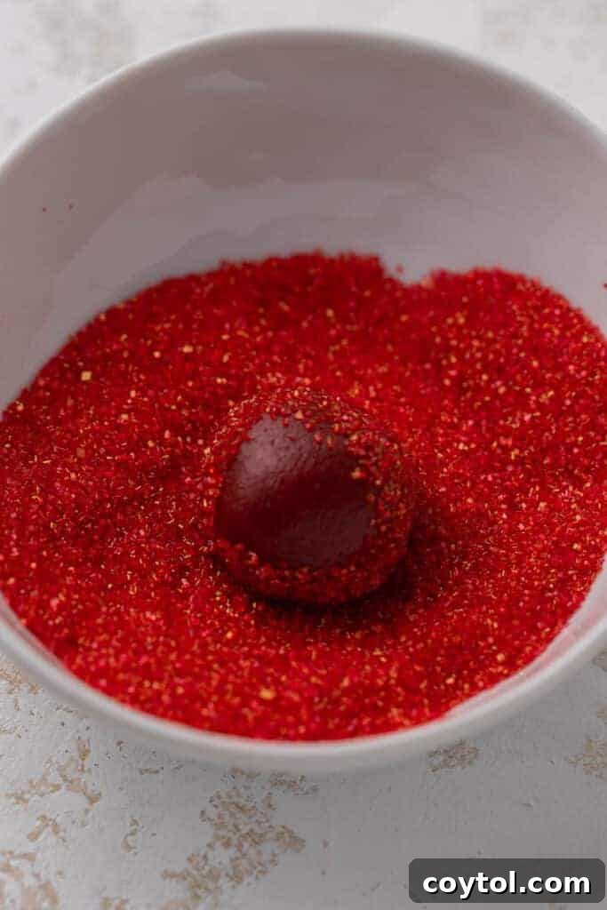 Red velvet cookie dough ball being rolled in red sanding sugar for a festive coating
