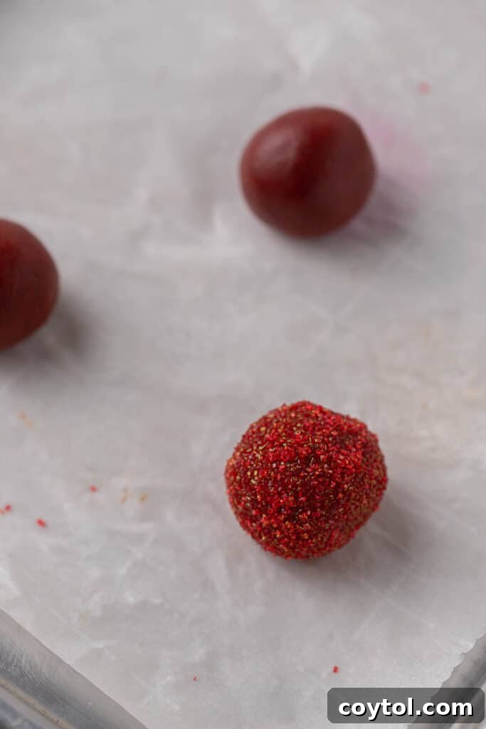 Red velvet cookie dough balls coated in red sugar on a baking sheet, ready for the oven