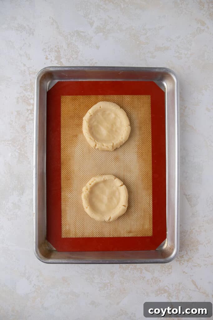 Crumbl's Sublime Chilled Banana Cream Pie Cookies 8 Cookie dough balls with wells pressed into them on a baking sheet, ready for the oven.