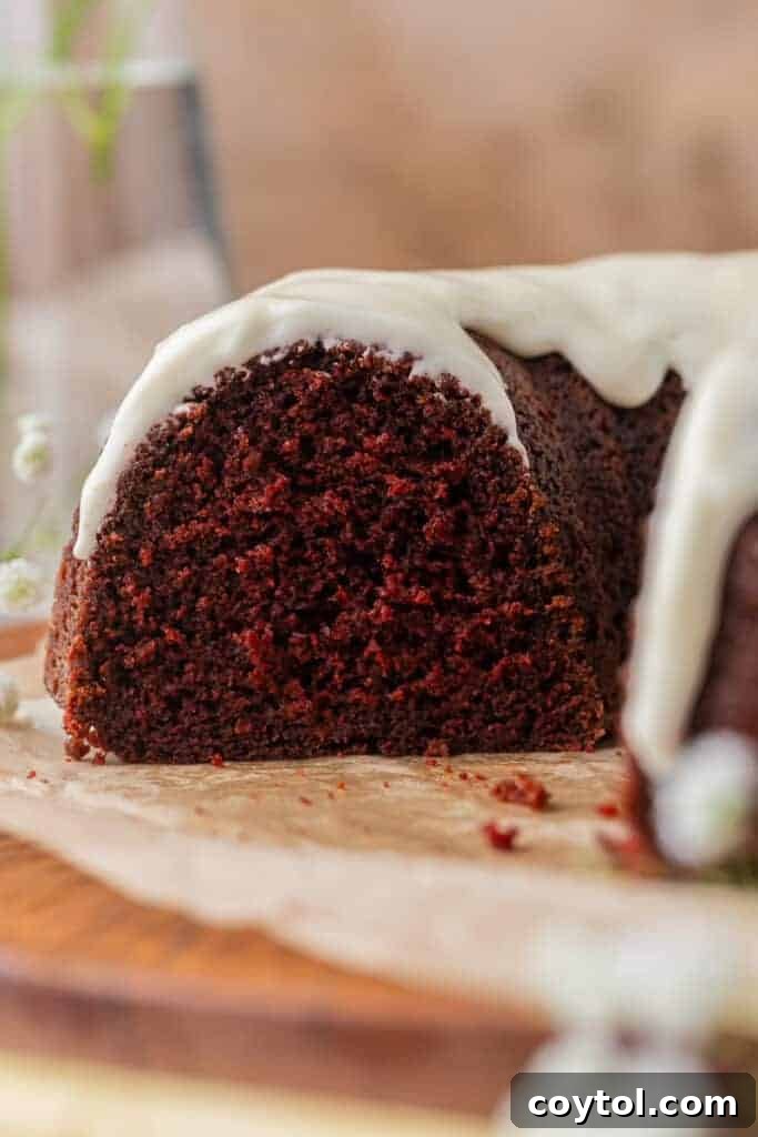 A beautifully sliced red velvet bundt cake, showcasing its moist texture and the generous cream cheese glaze on top.