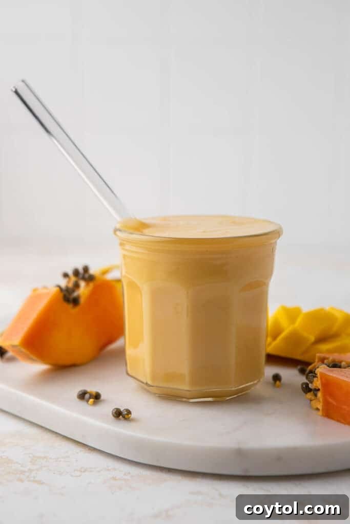 Delicious and creamy papaya mango smoothie in a glass with tropical fruit in the background.