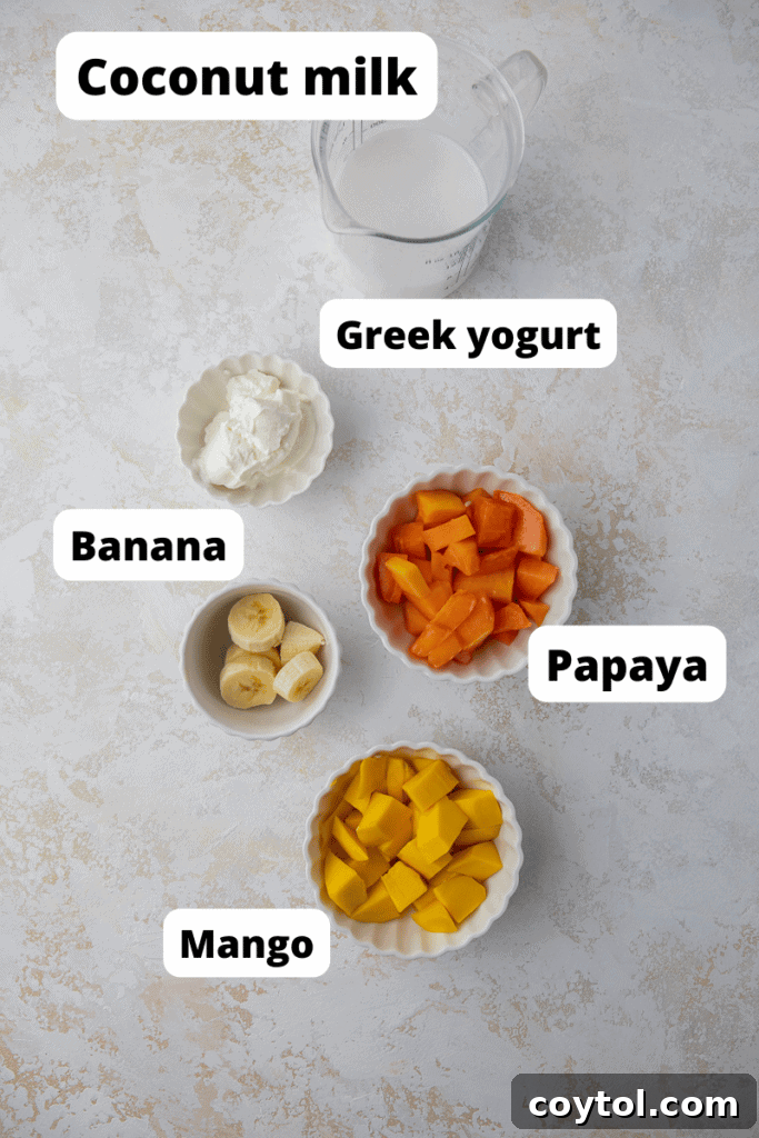 Ingredients for a healthy papaya mango smoothie laid out on a table, including sliced papaya, mango, banana, Greek yogurt, and coconut milk.