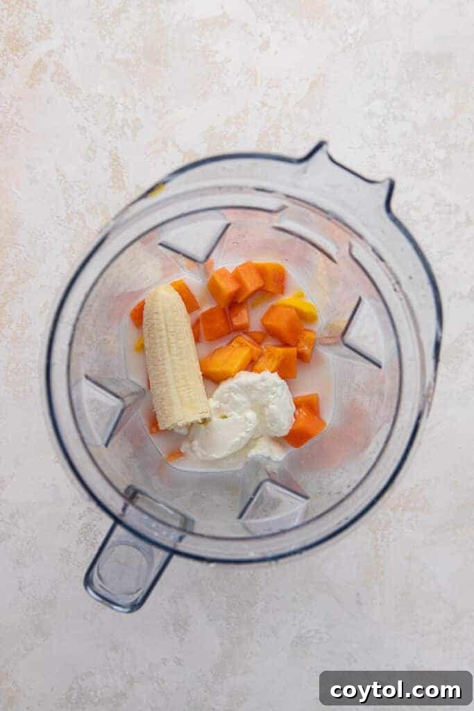 A blender filled with a vibrant mix of papaya, mango, and banana, ready to be blended into a smoothie.