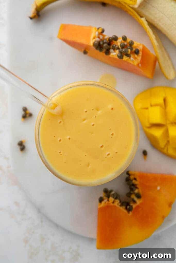 A vibrant, creamy tropical smoothie served in a tall glass, garnished with fresh fruit slices.