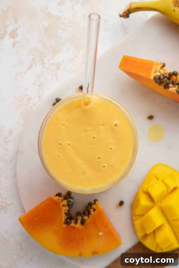 A high fiber tropical smoothie with papaya and mango, beautifully presented in a glass, with fresh ingredients in the background.