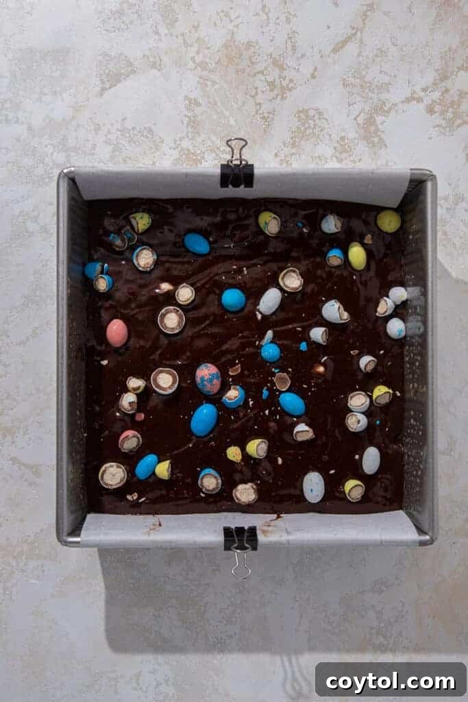Easter mini egg brownies baking in a parchment-lined sheet