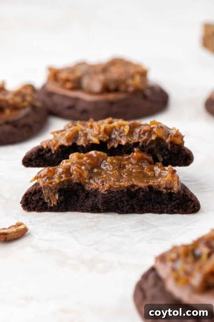 A Crumbl German chocolate cookie broken in half, revealing its moist chocolate interior and layers of frosting and drizzle.