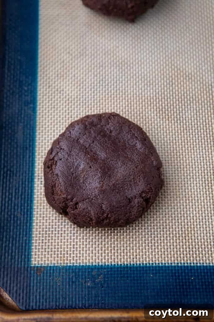 Chocolate cookie dough portions flattened on a parchment-lined baking sheet, spaced for even baking.
