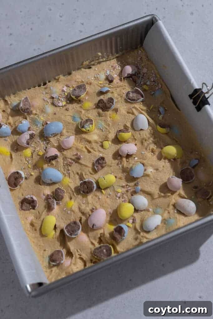 Blondie batter with Cadbury mini eggs spread evenly in a prepared baking pan