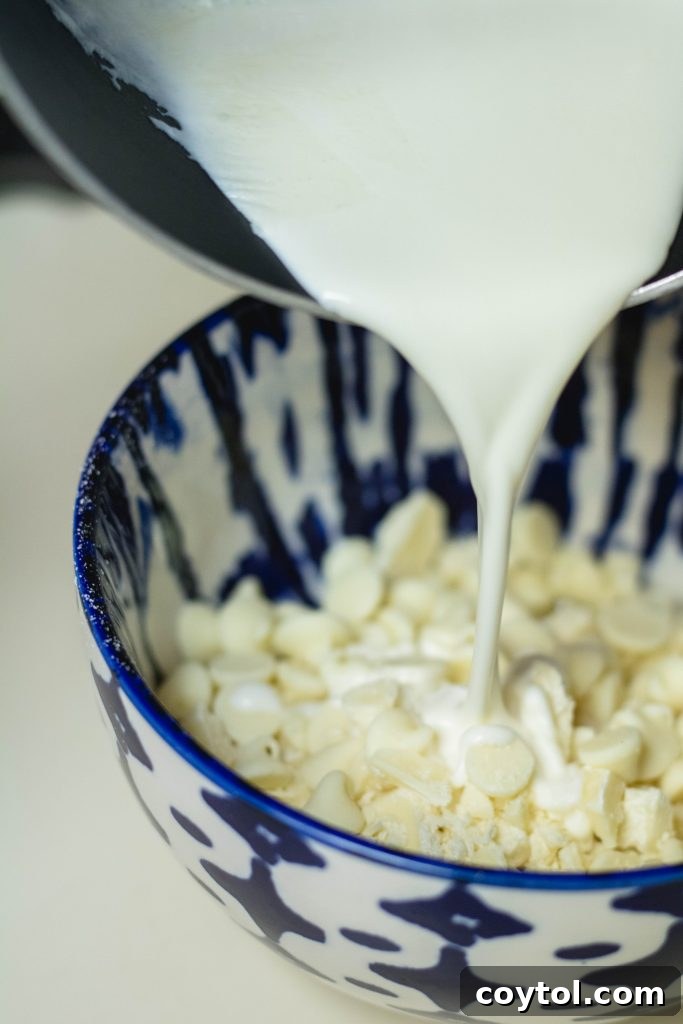 Pouring hot heavy cream over chopped white chocolate chips in a bowl