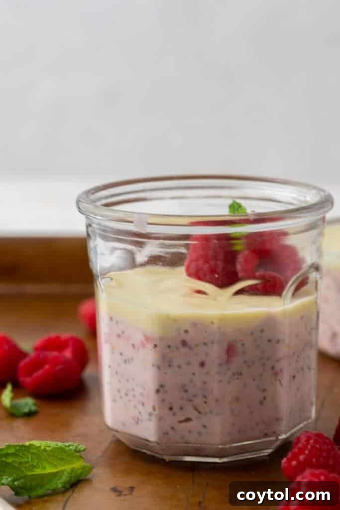 Close-up of layered overnight oats with raspberries and white chocolate in a cup, showing the vibrant colors.