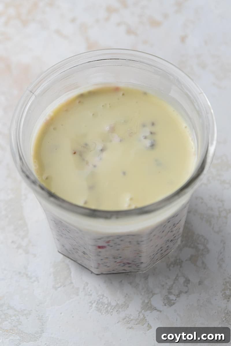 Melted white chocolate being poured over the mixed oatmeal in a cup.