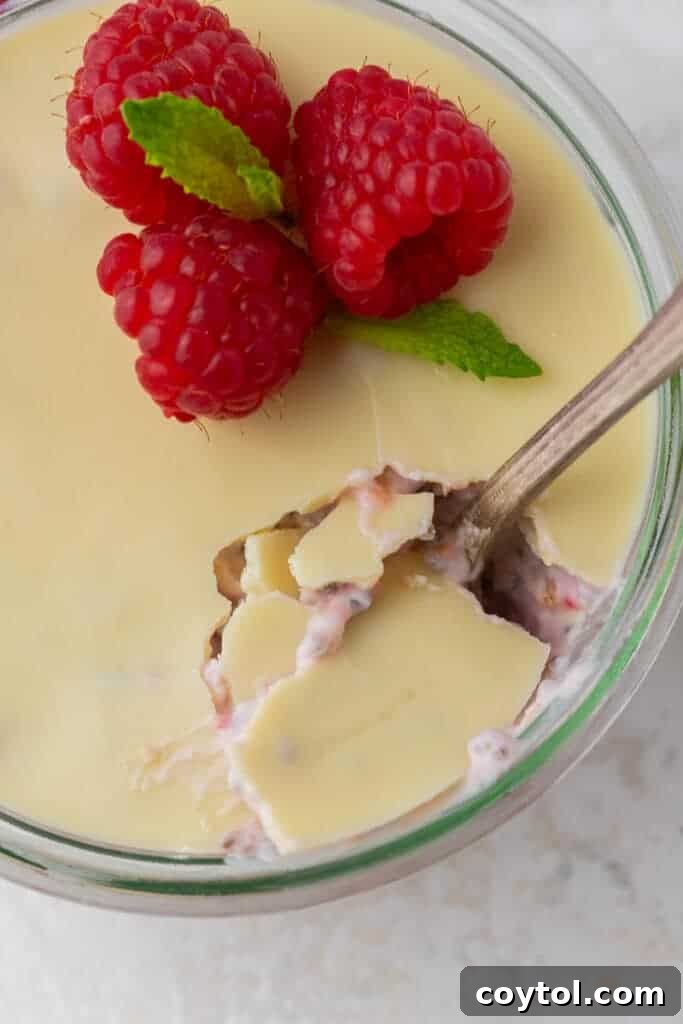 A spoon breaking through the hard white chocolate layer on top of raspberry overnight oats.
