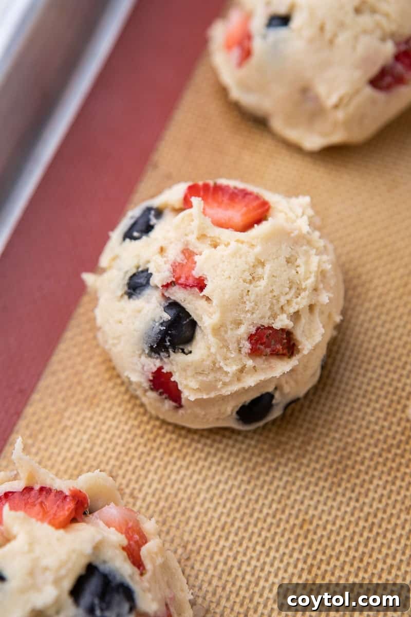 Scooped Berries and Cream cookie dough balls, flattened slightly, arranged on a parchment-lined baking sheet before baking.