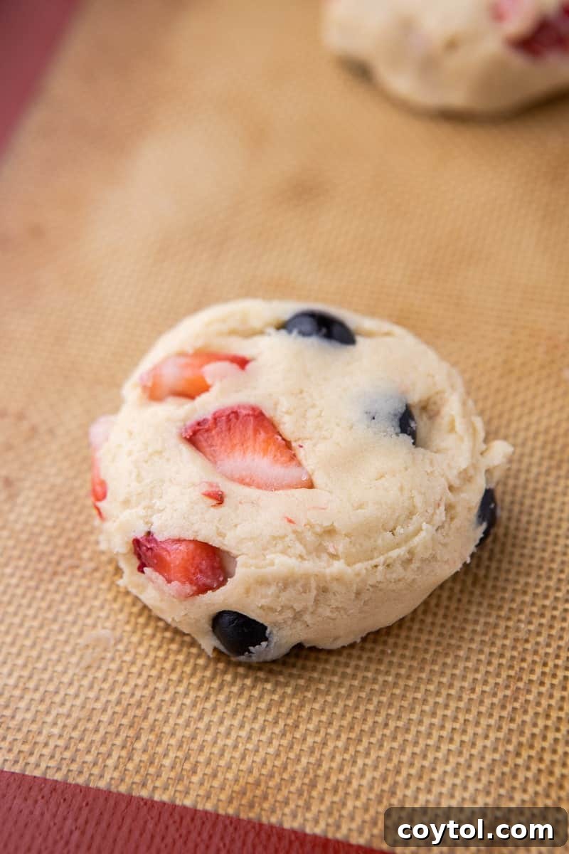Close-up of a single Berries and Cream cookie dough ball on a baking sheet, showing visible fruit pieces.