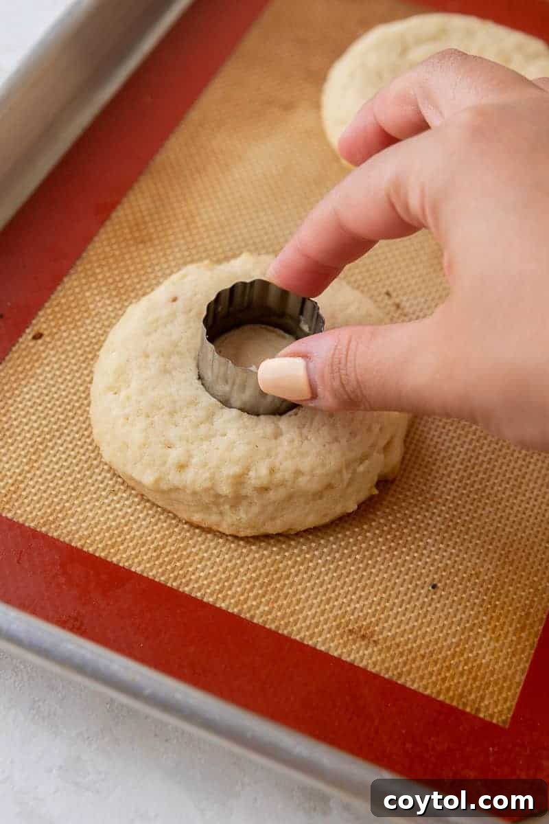 A hand using a small cookie cutter to remove the center of a baked cookie