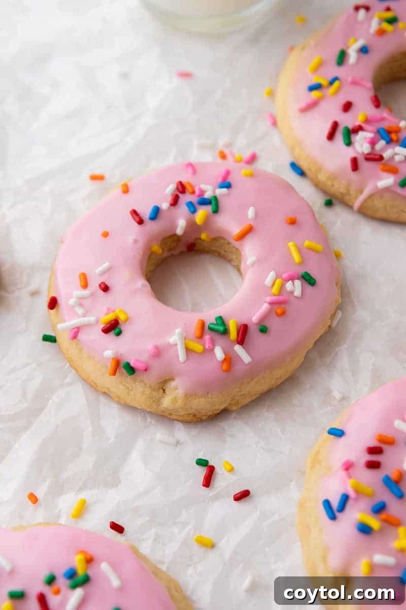 A batch of pink donut cookies covered in glaze and rainbow sprinkles