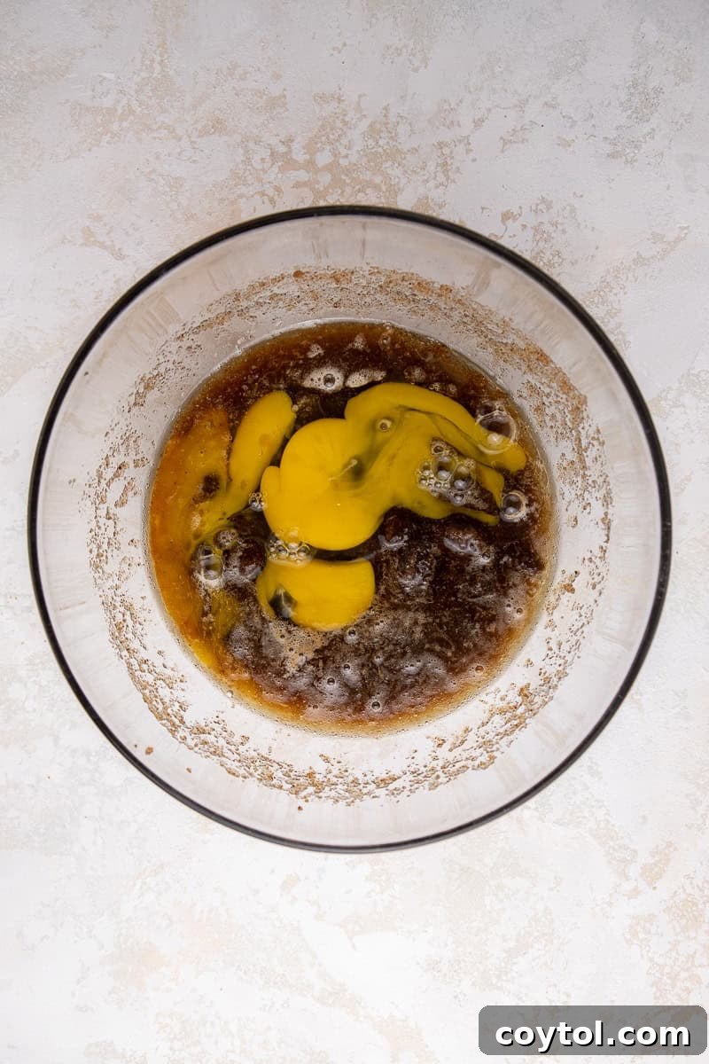 Wet ingredients (cooled brown butter, sugars, eggs, vanilla) mixed until light, pale, and fluffy in a large mixing bowl, showing optimal aeration.