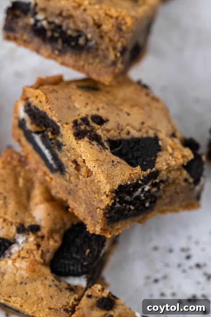 Single fudgy brown butter Oreo blondie square with visible cookie chunks and a slightly crinkly top, on a white background.