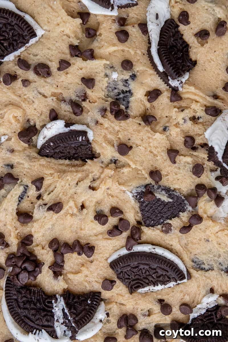 Simple Skillet Oreo Cookies and Cream Pizookie 7 Close-up of unbaked cookie dough in a skillet, topped with extra Oreos and chocolate chips.