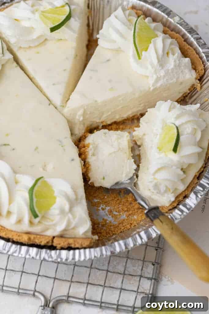 A slice of key lime pie on a white plate with a fork, showing the creamy texture and graham cracker crust.