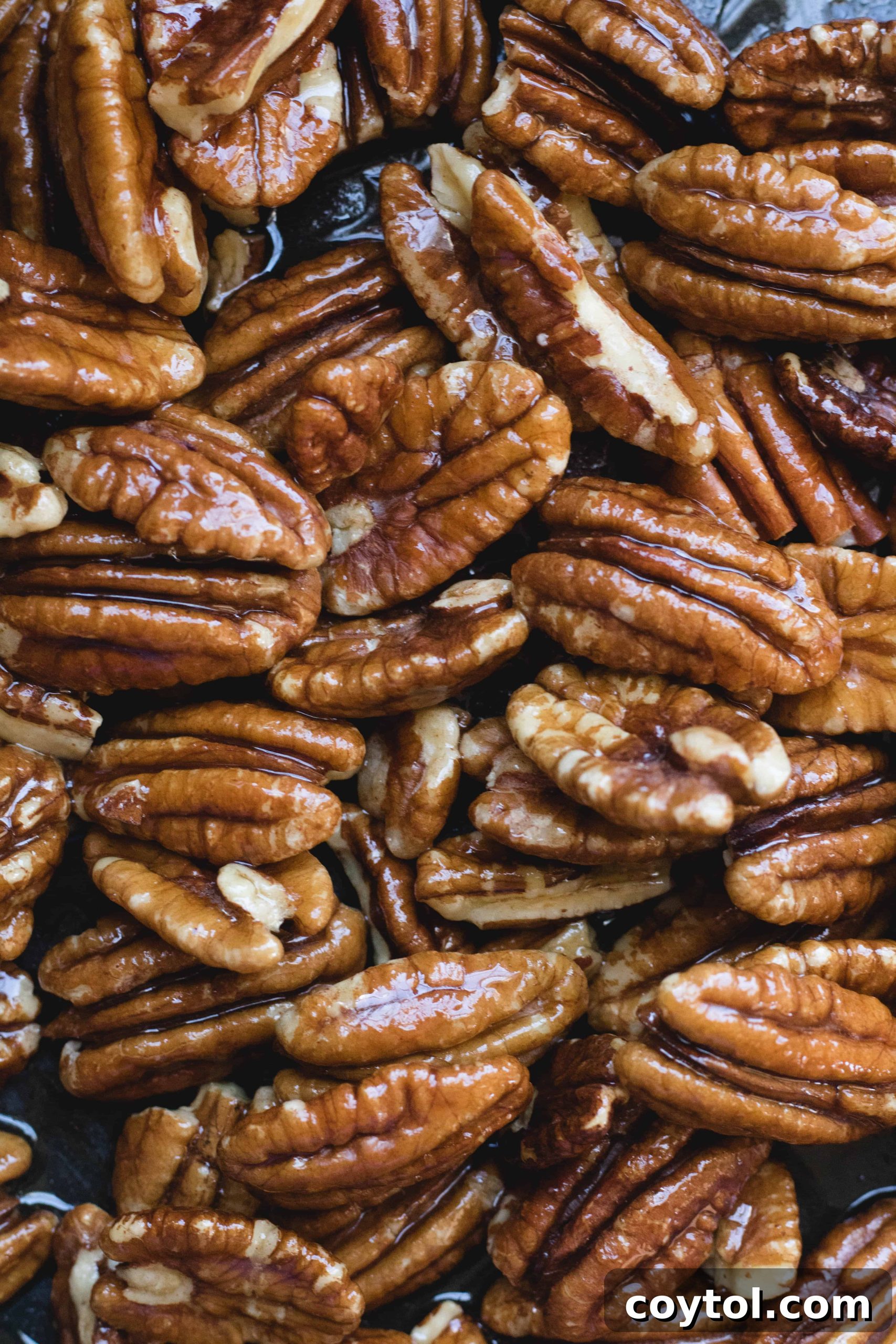 Maple syrup coated pecans cooking in a pan, achieving a beautiful golden hue for candied pecans.