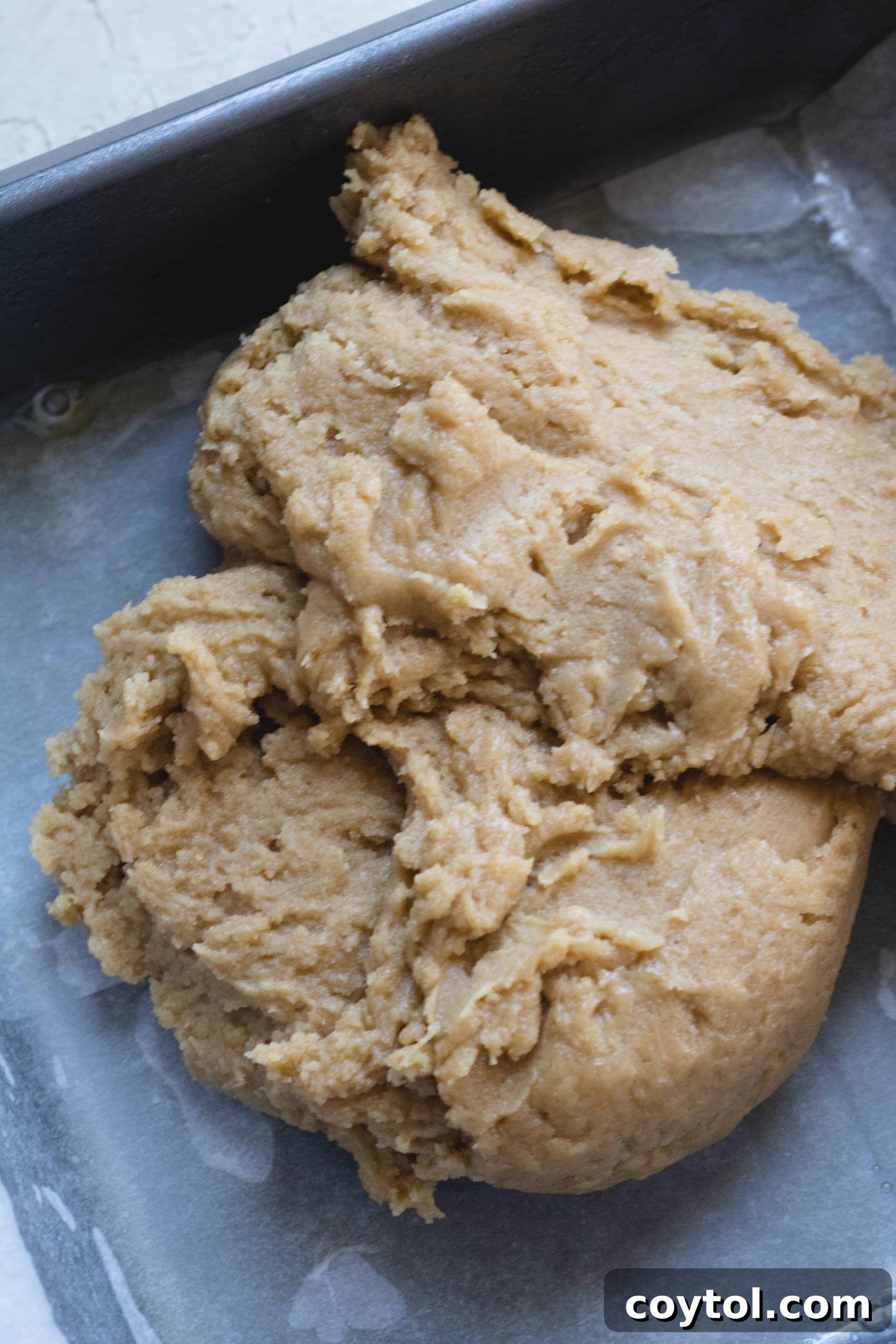 Blondie dough being flattened into the prepared baking pan with a spatula.