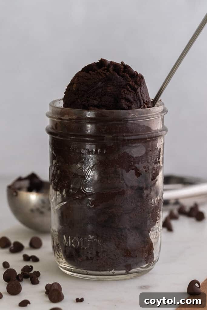 Edible brownie batter in a small glass jar, with a spoon digging into it